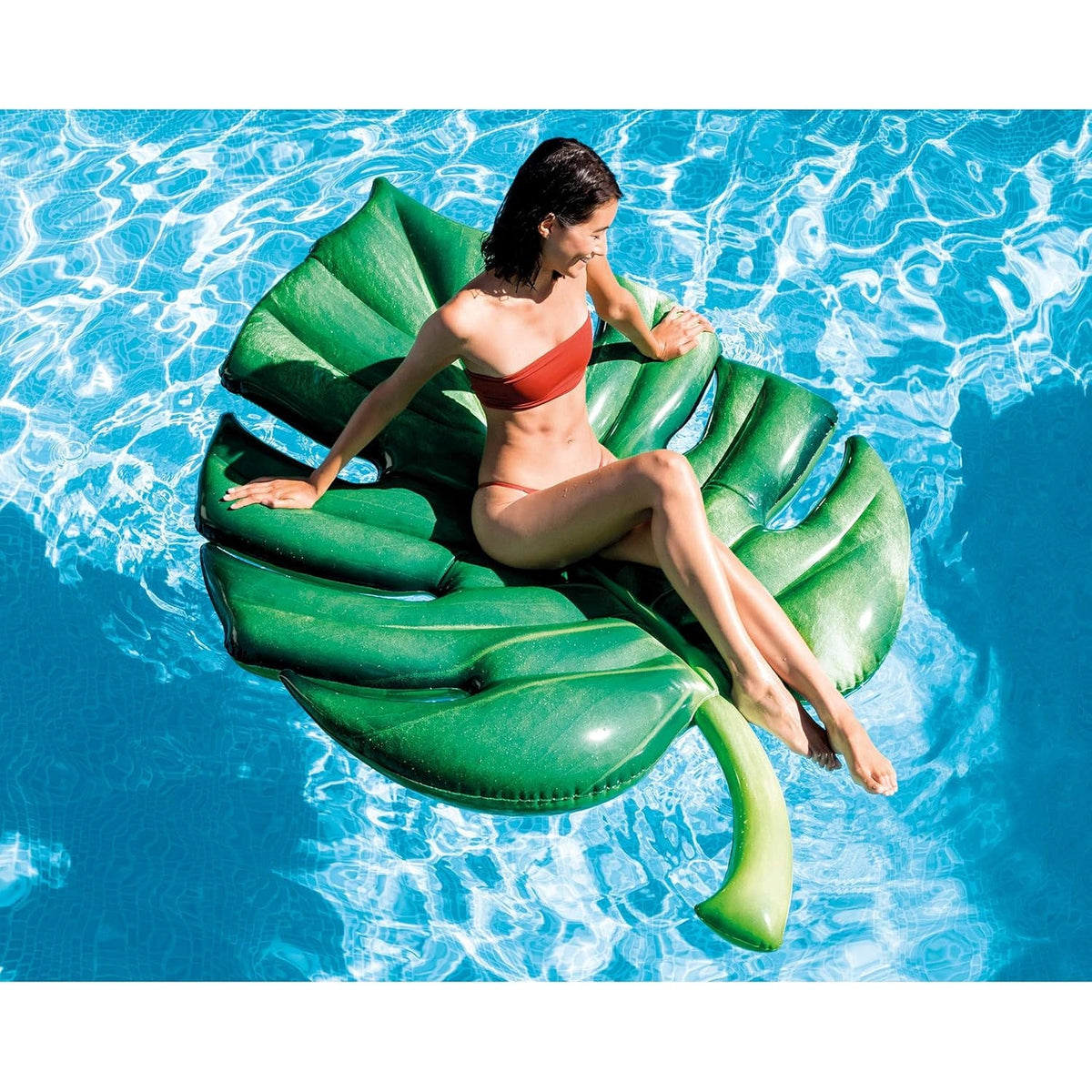 Aufblasbare Luftmatratze in Form eines tropischen Palmblatts, grün, mit einer Frau im roten Bikini auf der Wasseroberfläche schwimmend